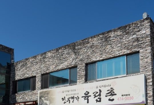 돌벽 2층 건물 외관과 간판 '한우명가 육림촌 · 예약문의 474-3030'